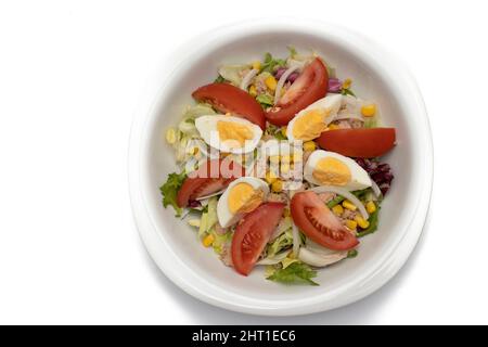 Salade mélangée dans un bol blanc. Ingrédients laitue, maïs, oignon, thon, tomates, œufs, huile d'olive, chou rouge. Concept alimentaire méditerranéen. Banque D'Images