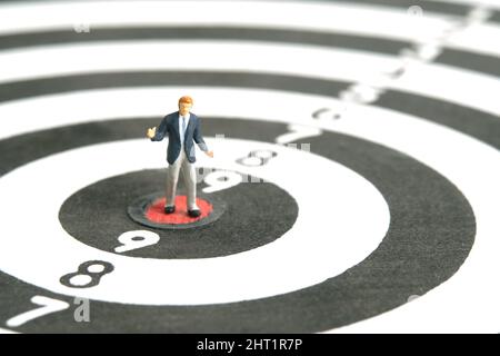 Photographie miniature de personnage de jouet de personnes. Un homme d'affaires haussant debout au centre du dartboard. Isolé sur fond blanc. Photo d'image Banque D'Images