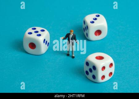 Photographie miniature de personnage de jouet de personnes. Un homme d'affaires haussant debout au milieu des dés blancs. Isolé sur fond bleu. Photo d'image Banque D'Images