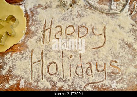 Happy Holidays écrit du texte dans la farine, sur le comptoir, avec emporte-pièce en métal pour pain d'épice, pour la cuisson des biscuits de Noël, Browntown, Wisconsin USA Banque D'Images