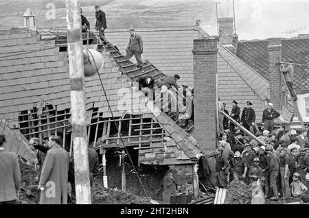 Aberfan - 21st octobre 1966 mineurs, villages et services d'urgence, sur le toit de l'école Pantans Junior, espérant des signes de vie ci-dessous. Ils finiront par frapper ce toit vers le bas pour obtenir un meilleur accès à la boue en dessous. Le désastre d'Aberfan a été l'effondrement catastrophique d'un pourboire de collierie dans le village gallois d'Aberfan, près de Merthyr Tydfil. Elle a été causée par une accumulation d'eau dans la roche accumulée et le schiste, qui a soudainement commencé à glisser en descente sous forme de lisier et a englouti la Pantglas Junior School ci-dessous, le 21st octobre 1966, tuant 116 enfants et 28 adultes. Le Banque D'Images