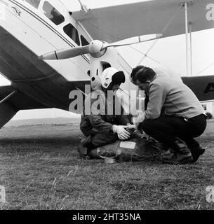 La recherche aérienne du bateau de plaisance manquant Darlwyne. Un hélicoptère naval atterrit de l'équipement de sauvetage à l'aéroport de St Just pour les avions de recherche. Le pilote de l'hélicoptère explique l'utilisation de l'équipement à l'un des pilotes de recherche. Le Darlwyne s'est coulé le 31st juillet 1966, ce qui a entraîné la perte de 31 vies et l'épave du bateau n'a jamais été trouvée. Les cadavres de seulement 12 des 31 personnes à bord ont jamais été récupérés. 5th août 1966. Banque D'Images