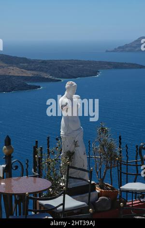 Santorin, Grèce : 10 mai 2021 : vue imprenable depuis une terrasse de restaurants avec tables, chaises et une statue grecque sur la mer Égée à Santorin Banque D'Images