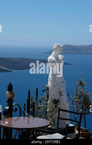 Santorin, Grèce : 10 mai 2021 : vue imprenable depuis une terrasse de restaurants avec tables, chaises et une statue grecque sur la mer Égée à Santorin Banque D'Images