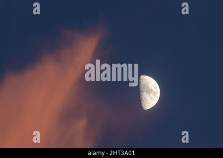 Gros plan d'une demi-lune au coucher du soleil avec des nuages rouges Banque D'Images