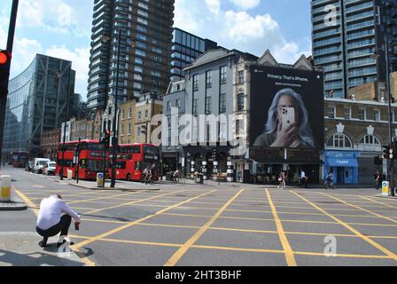 Un londonien se dédort et utilise son téléphone pour prendre une photo d'une publicité à grande échelle pour les Apple i-phones à Shoreditch, dans l'est de Londres. Banque D'Images