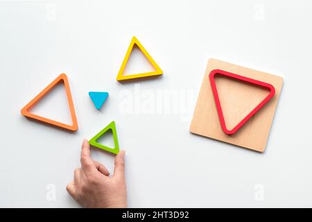 Triangles en bois imbriqués peints dans des couleurs arc-en-ciel. Pose à plat sur fond de papier blanc. Banque D'Images