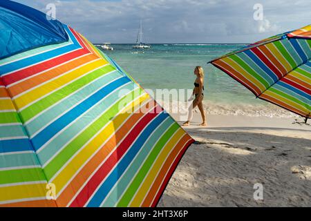 Une jeune femme blonde se balade le long de la mer entre des parasols de plage colorés à Akumal, au Mexique Banque D'Images
