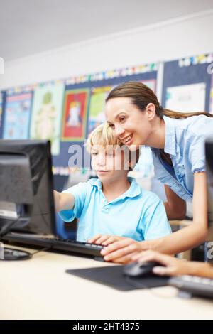 Poser des questions en classe informatique. Un jeune enseignant attrayant assistant un écolier en classe informatique. Banque D'Images