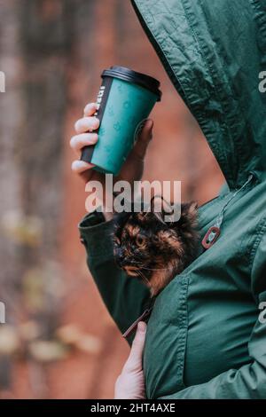 Photo verticale d'une femme avec une tasse à emporter tenant un chat tortoiseshell Banque D'Images