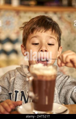 Photo verticale d'un enfant du Caucase qui boit du lait au chocolat dans un café Banque D'Images