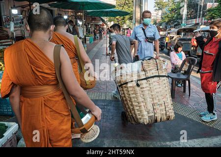 Un ouvrier du marché avec chariot, un migrant de Myanmar, se précipitant pour sortir de la voie de deux moines bouddhistes; Pak Klong Talat (marché), Bangkok, Thaïlande Banque D'Images