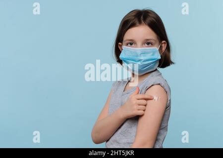 Enfant fille dans un masque protecteur montrant un patch de plâtre sur le bras après la vaccination contre l'infection COVID-19. Enfant vacciné contre Covid-19. Enfants Covid 19 prévention. Concept de soins de santé et de médecine Banque D'Images