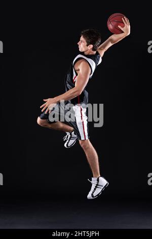 HES a obtenu des superpuissances de basket-ball. Photo pleine longueur d'un jeune joueur de basket-ball masculin en action sur fond noir. Banque D'Images