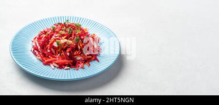 Salade de betteraves au chou et aux carottes dans une assiette bleue sur fond gris. Banque D'Images