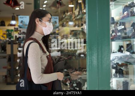 Jeune femme asiatique portant un masque pour regarder une vitrine de la boutique de chaussures. Banque D'Images