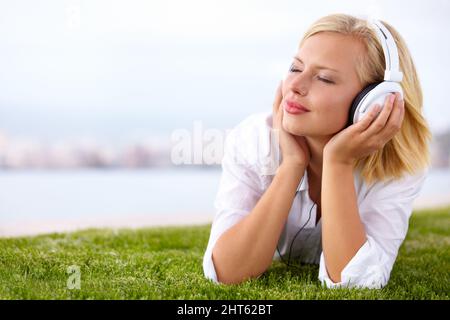 Emportant sa musique partout Prise de vue d'une femme allongé sur un terrain herbacé écoutant de la musique avec ses yeux fermés. Banque D'Images