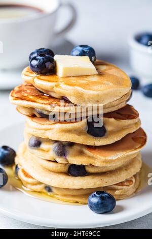 Une pile de crêpes aux myrtilles avec du sirop d'érable et du beurre sur une assiette de petit-déjeuner blanche. Banque D'Images