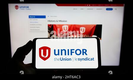 Personne tenant un téléphone cellulaire avec le logo du syndicat général canadien Unifor à l'écran devant la page Web. Mise au point sur l'affichage du téléphone. Banque D'Images