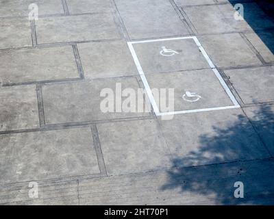L'ancien symbole d'icône pour handicapés blanc au sol montre une pancarte réservée aux personnes handicapées dans une place de parking, vue de dessus. Banque D'Images