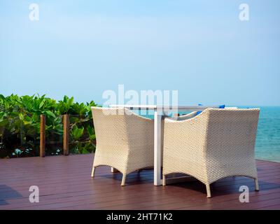 Mobilier moderne en rotin blanc vide, table de jardin extérieure tissée avec table et trois chaises sur la terrasse sur la plage avec vue sur la mer et ciel bleu Banque D'Images