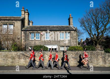 Les membres du groupe de reconstitution militaire du Régiment de foot de sa Majesté en 33rd, traversent le village de Golcar, dans la vallée de Colne, dans le Yorkshire, avant d'assister à une apparition à la journée des Golcar Havercakes, au musée de la vallée de Colne, à Huddersfield. Date de la photo: Dimanche 27 février 2022. Banque D'Images