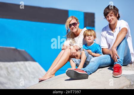 Lui apprendre à styliser. Portrait de deux jeunes adolescents et d'un petit garçon assis à l'extérieur d'un parc de skate. Banque D'Images