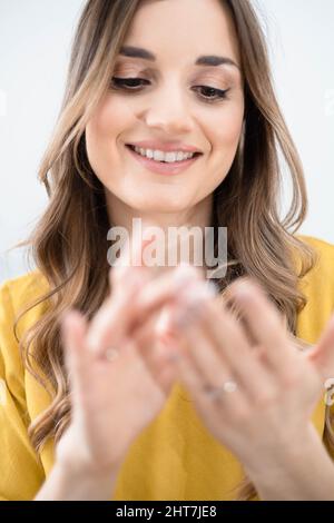 La jeune femme brune utilise de la crème cosmétique, regardant ses mains Banque D'Images