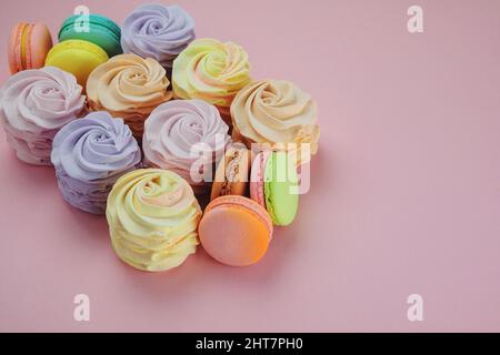 Variété de bonbons : macarons, guimauves et zéphans sur fond rose, gros plan. Desserts sucrés traditionnels colorés pour les vacances, espace copie. Banque D'Images