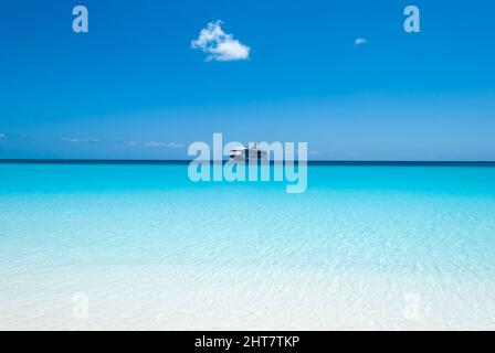 Vue sur les eaux transparentes et colorées de la plage Half Moon Cay et un bateau de croisière dérivant en arrière-plan (Bahamas). Banque D'Images