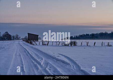 Paysage hivernal d'une route enneigée avec taches de roue de voiture au coucher du soleil Banque D'Images