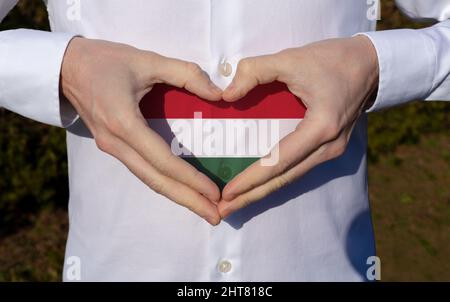 homme qui tient ses mains dans le coeur en forme de chemise blanche avec drapeau hongrois couleurs tricolores symbole de la journée nationale hongroise 15th de mars . Banque D'Images