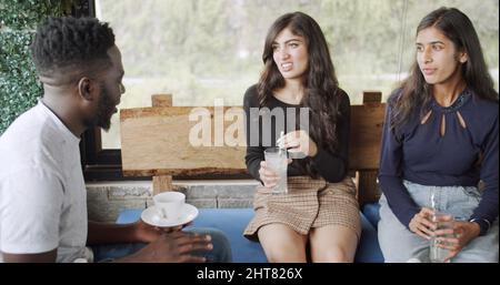 Jeunes femmes d'Asie du Sud ayant une discussion sérieuse assis dans un café avec un gars Banque D'Images