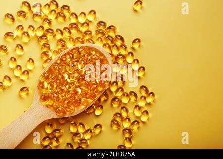 Capsules de vitamine D3 dans une cuillère avec d'autres capsules de vitamine D3 autour d'elles sur fond jaune. Anciennes capsules avec un supplément alimentaire pour les articulations te Banque D'Images