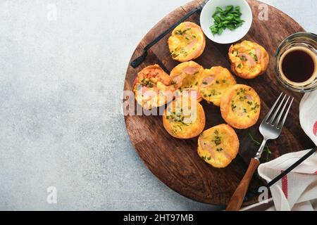 Délicieux muffins aux œufs avec oignons verts, bacon, fromage et tomates sur panneau de bois sur fond clair. Petit déjeuner sain à teneur élevée en protéines et faible en glucides. Banque D'Images