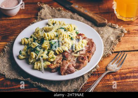 Steak de porc avec pâtes crémeuses aux épinards, garni de fromage râpé Parmesan sur plaque blanche Banque D'Images