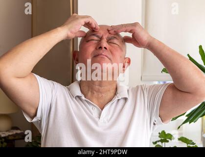 Un homme âgé mûr à la maison pinçant et frottant sa tête se sentant mal et ou dans la douleur. Concept de malaise. Banque D'Images