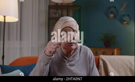 Grand-père senior homme regardant à travers la loupe, la lecture, la recherche, l'examen à la maison Banque D'Images