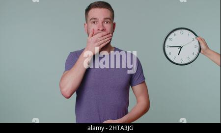 Homme confus avec anxiété de vérifier l'heure sur l'horloge, courir tard au travail, étant dans le retard, échéance Banque D'Images