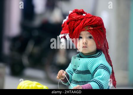 Bébé asiatique du Sud portant un chandail d'hiver vert et un turban rouge debout sur un cheval jouet Banque D'Images