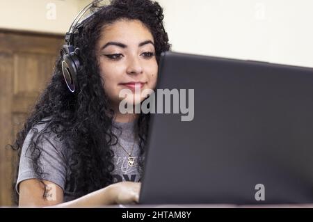 Gros plan sur une jeune femme hispanique qui travaille sur son ordinateur portable tout en portant un casque Banque D'Images