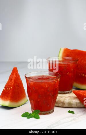 Boisson glacée à la pastèque servie sur un verre transparent sur fond blanc isolé. Mise au point sélective avec tranches de fruits de pastèque. Copier l'espace pour le texte. Banque D'Images