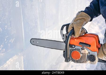 Fabrication de sculptures sur glace. Un homme coupe la surface dans un bloc de glace avec une scie à essence sur le lac Baikal. Banque D'Images