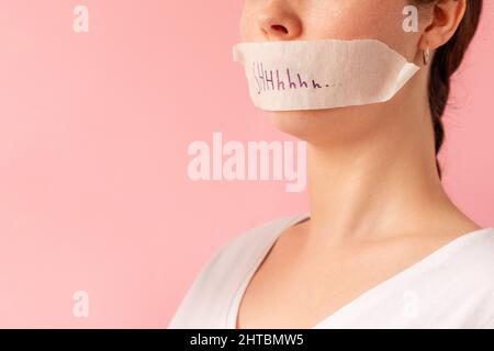 Portrait d'une femme de race blanche avec sa bouche fermée par ruban adhésif. La bande porte l'inscription Shhh. Fond rose. Le concept des secrets et des problèmes des femmes. Banque D'Images