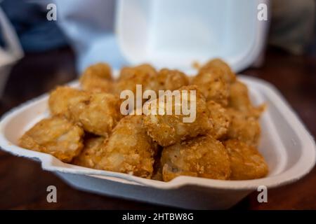 Sélection de tots de cratère croustillants et dorés dans un contenant de styromousse blanc à emporter d'un restaurant. Banque D'Images