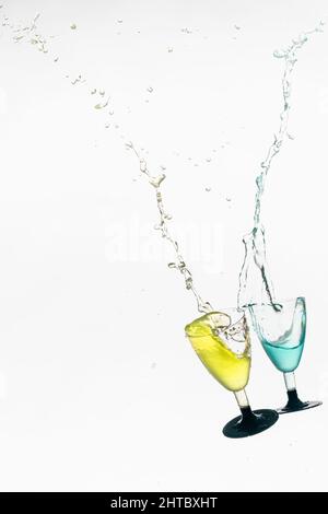 Collision de deux verres avec des liquides colorés avec des éclaboussures d'eau du verre sur un fond blanc Banque D'Images