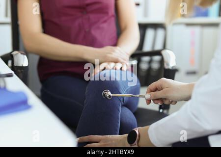 Médecin neurologue vérifiant les réflexes du genou de la patiente avec marteau à percussion en clinique Banque D'Images