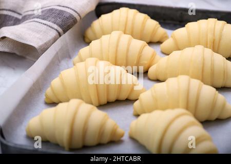 Gros plan d'un rouleau de pâte de croissants français traditionnels non cuits au levain dans une plaque de cuisson et une feuille de papier, en préparation de la cuisson au four. Il Banque D'Images