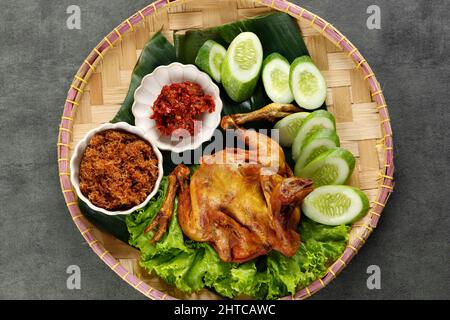 Ayam Goreng Kelapa Parut ou poulet frit avec de la noix de coco déchiquetée avec du concombre, cuisine traditionnelle indonésienne, servi dans une assiette de bambou brun. Ayam Serunde Banque D'Images