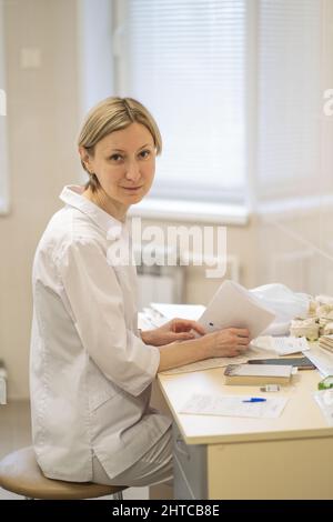 Une femme médecin remplit les documents administratifs tout en étant assise à un bureau dans son bureau. Banque D'Images